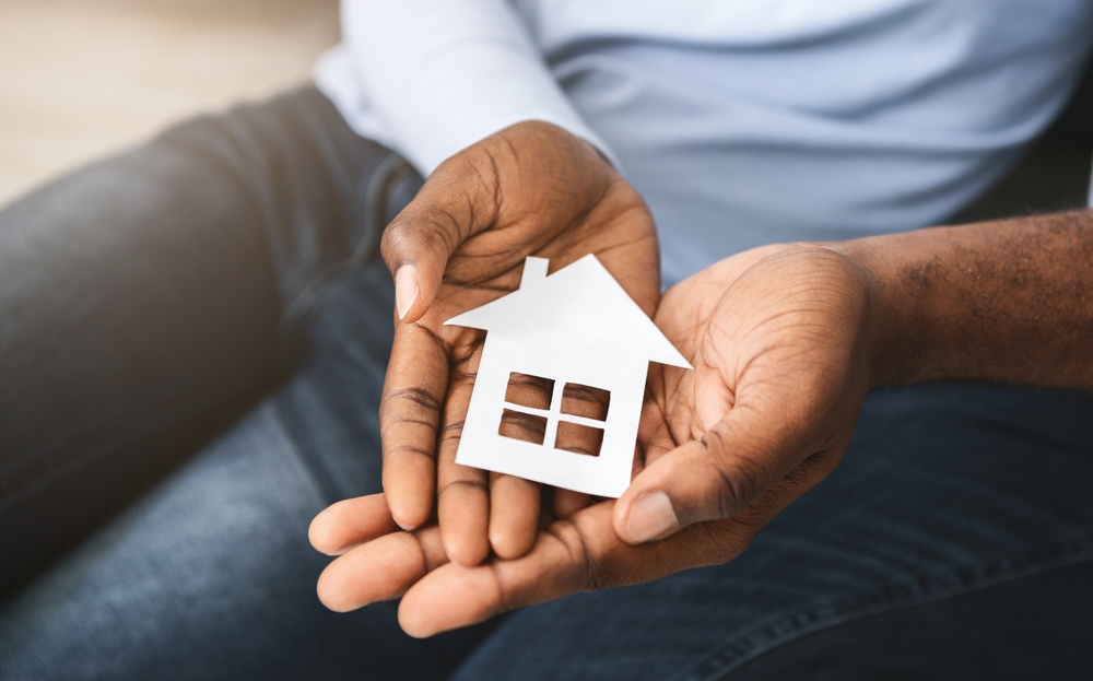 A photo of two people sitting next to each other, holding a cardboard cutout of a house, representing renting a home together.